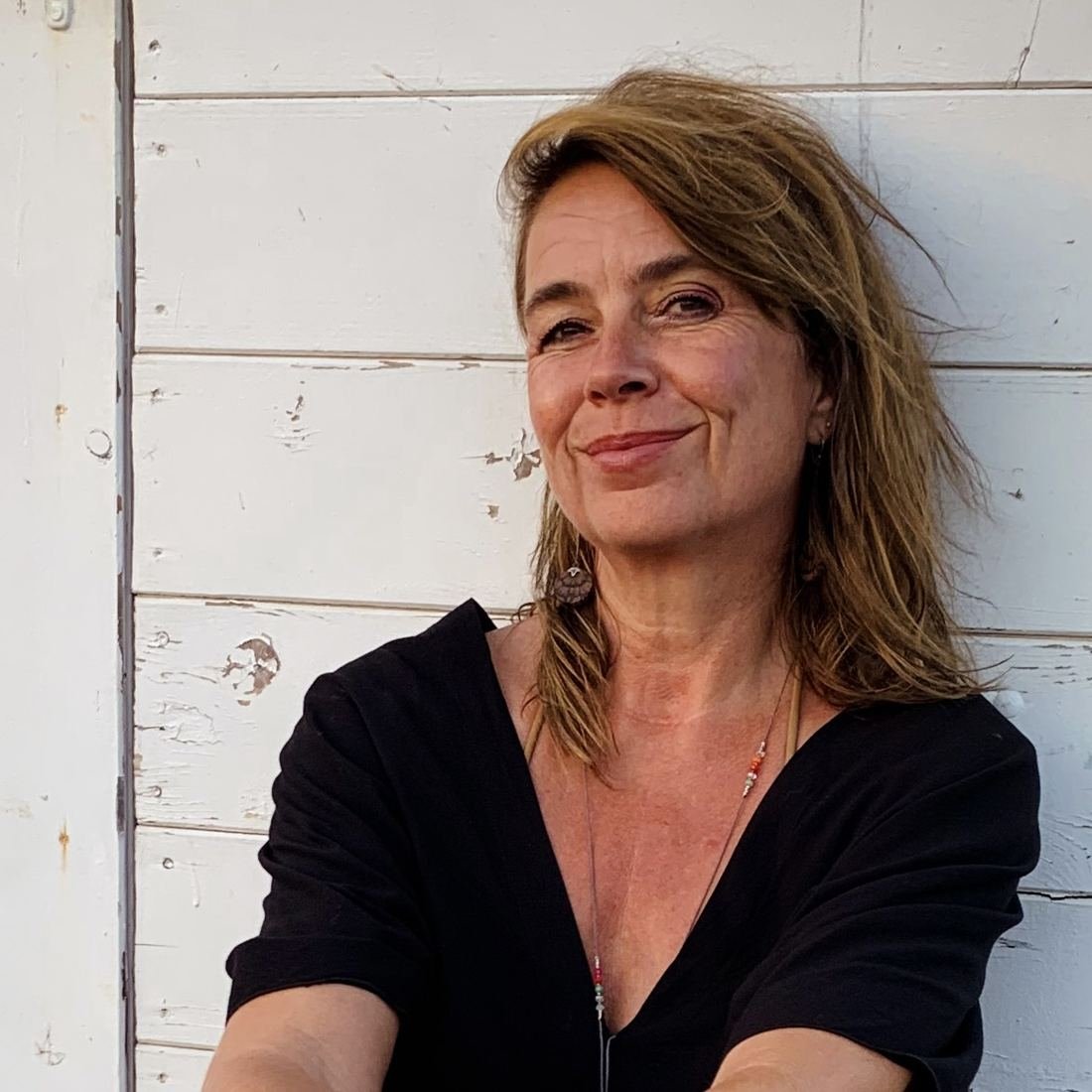 Elke Bayer smiling in front of a white wooden wall